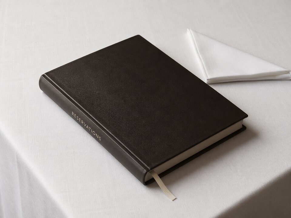 A single leather reservation book on pressed white linen